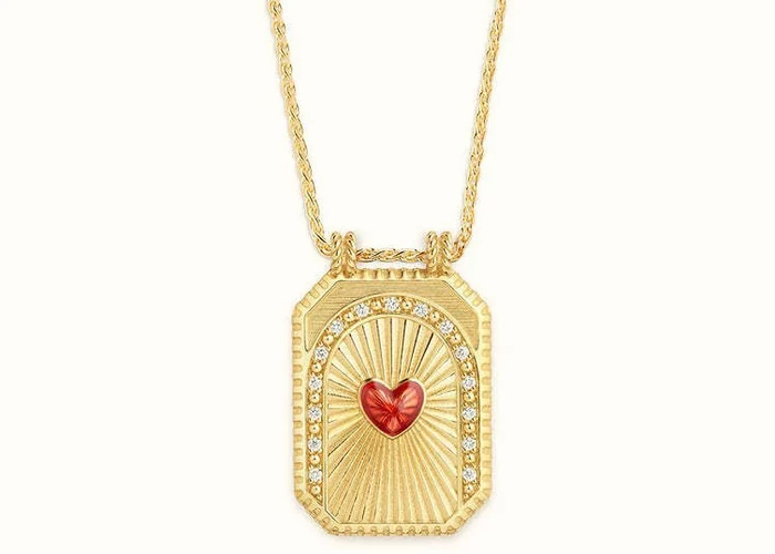 A large enamel heart tarot amulet on a gold chain, worn at the collarbone.