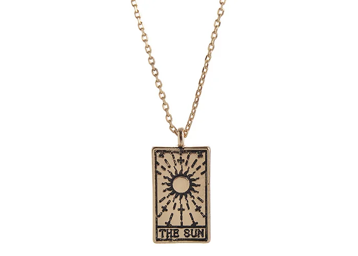 Engraved brass tarot pendants on fine chains, arranged on a pale cloth.
