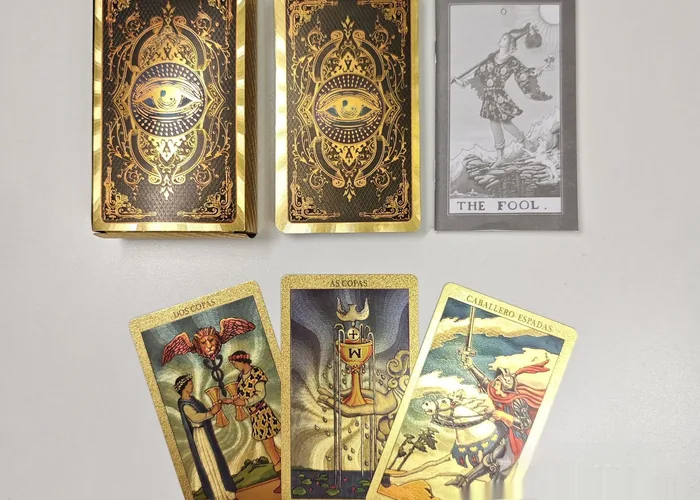 Two gold foil tarot boxes with an eye design, and three gold edged cards fanned out below them.