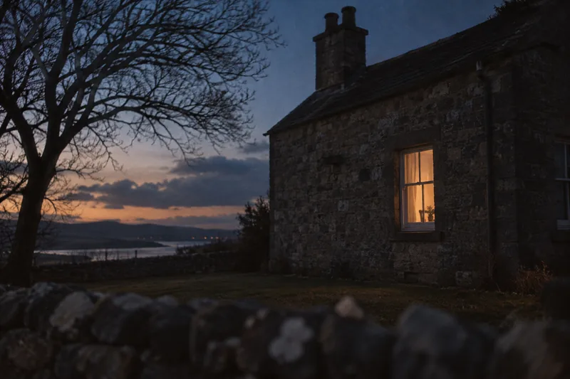 A single warm lit window in a dark house seen from the yard at dusk
