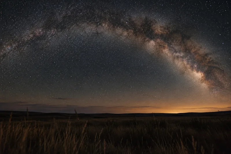The Milky Way arching over a dark prairie horizon at night